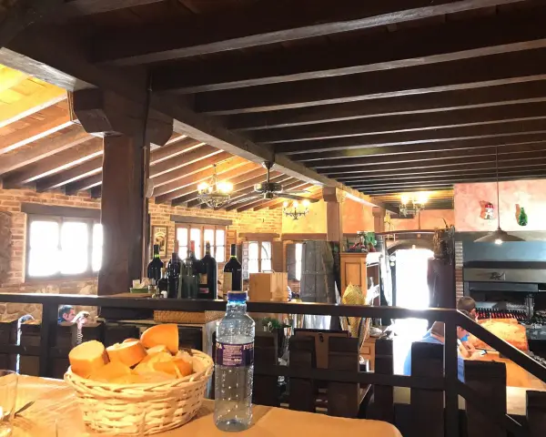 Interior rústico de restaurantes en Llanes, con vigas de madera, ladrillo y una parrilla a la vista. Cesta de pan y botella de agua en primer plano.