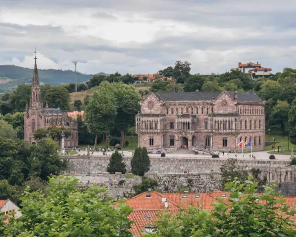 Edificio neogótico y palacio en Comillas, rodeados de vegetación y colinas. Un lugar para ver y disfrutar.