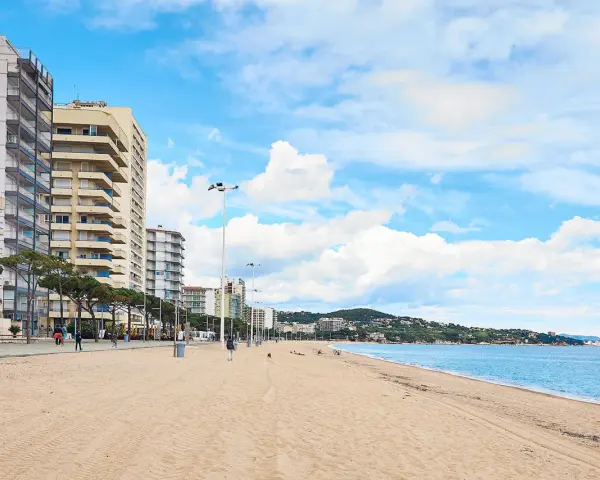 Amplia playa de arena dorada en la playa de Aro centro, con edificios altos a la izquierda y el mar azul a la derecha.