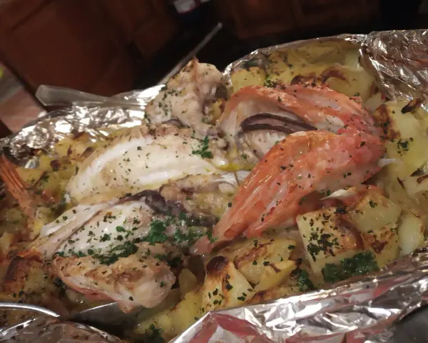 Delicioso pescado y gambas al horno con patatas, un plato típico de la casa Juanita Begur.