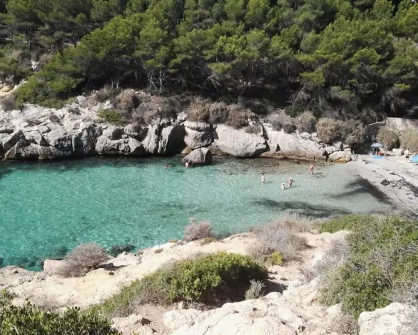 Es caló de la bella dona, una cala escondida con aguas turquesas y rocas escarpadas, donde algunos bañistas disfrutan del sol y el mar.