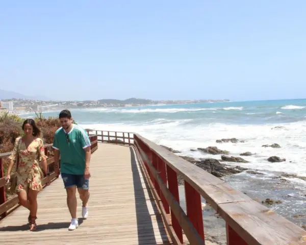 Pareja paseando por un sendero de madera con vistas al mar y la costa de Mijas. ¡Un lugar ideal que ver en Mijas Costa!