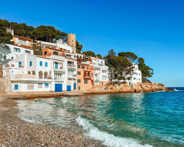Pueblo blanco en la costa, ideal para tu guía Costa Brava. Casas blancas y naranjas con vistas al mar turquesa.