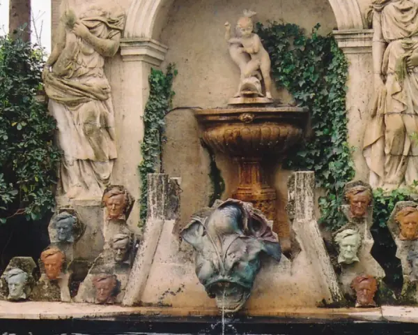 Fuente con estatuas y cabezas de piedra, evocando un antiguo castillo de gala.