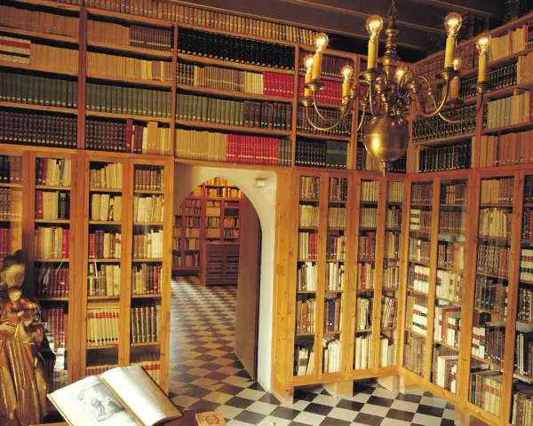 Interior del museu del castell de Peralada, con estanterías repletas de libros antiguos y una lámpara de araña dorada.