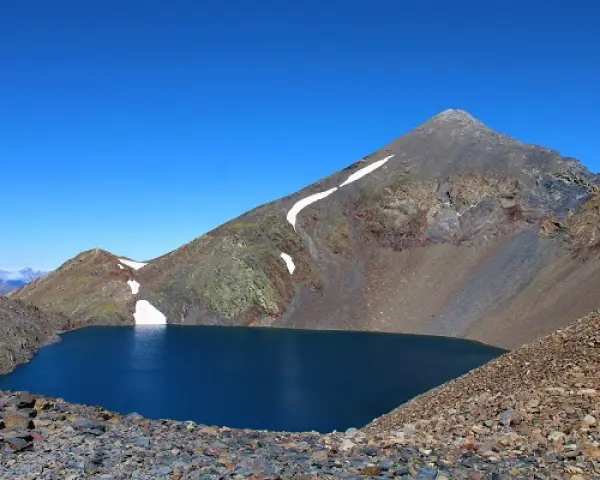 Lago azul profundo en el collado de Tebarray, rodeado de montañas rocosas y con restos de nieve.