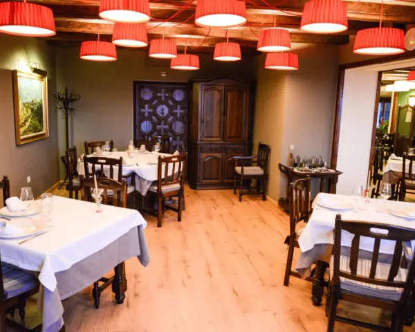 Mesas puestas y listas para comer en Morella. El restaurante tiene lámparas rojas, muebles de madera oscura y un cuadro en la pared.