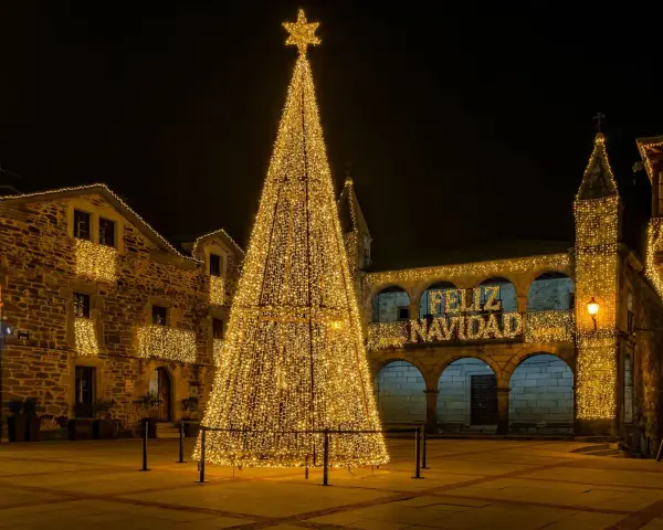 Árbol de Navidad gigante iluminado en una plaza, con edificios adornados y el mensaje "Feliz Navidad". Un lugar ideal que visitar en Navidad en España.