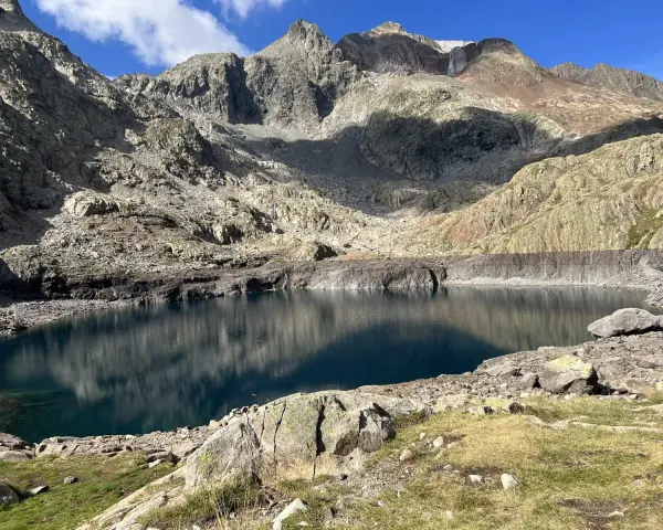 Un lago de montaña de aguas azules profundas, reflejando las cumbres rocosas y el cielo. Un paisaje perfecto para la ruta ibones azules.