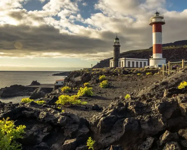 Faros gemelos en la costa rocosa, un destino que ver en La Palma. El mar y el cielo nublado completan la escena.