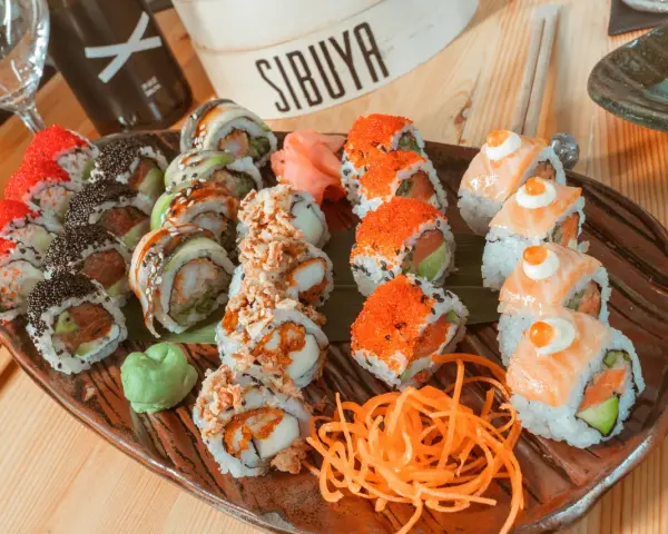 Variedad de sushi en plato marrón, ideal para saber donde comer en Vitoria. Incluye rollos con salmón, huevas de pez volador, aguacate y tempura.