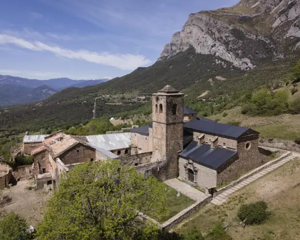 El monasterio de San Victorián, un conjunto de edificios de piedra con tejados oscuros, se alza majestuoso ante una imponente montaña rocosa.