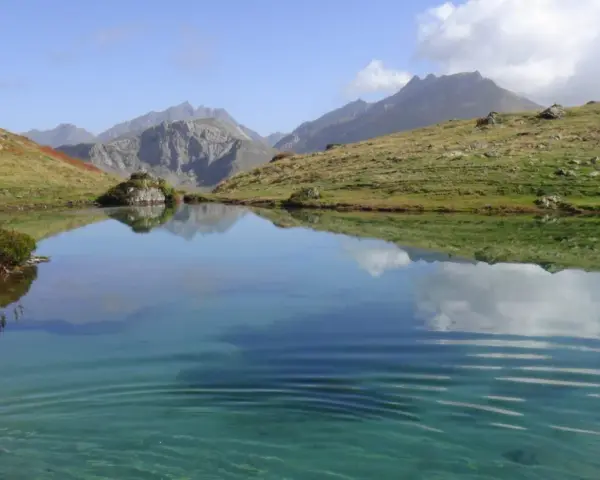 Un sereno ibón de espelunciecha refleja montañas y cielo azul.