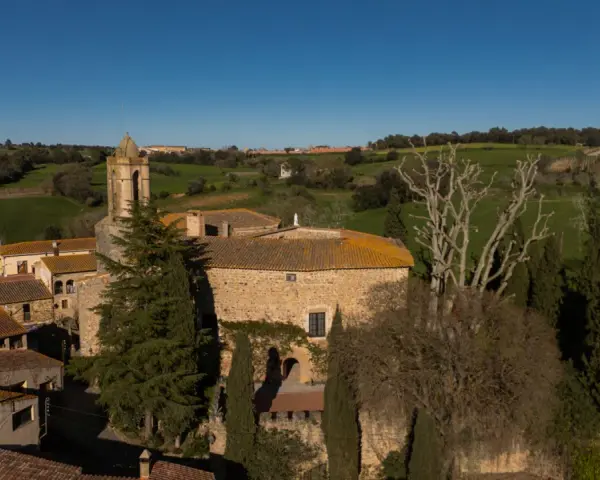 El castell de Gala, con su torre campanario, se alza entre tejados y vegetación, rodeado de verdes colinas bajo un cielo azul.