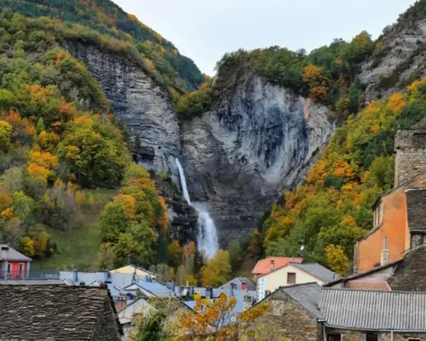 Cascada espectacular en Broto, Huesca, rodeada de bosques otoñales y casas de piedra.