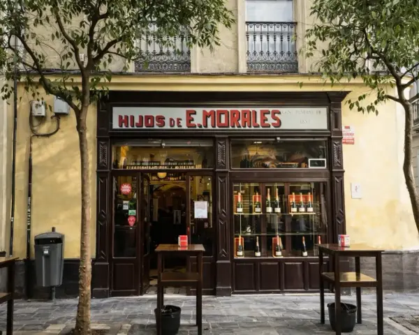 Fachada de "Hijos de E. Morales", un bar tradicional en Sevilla, con mesas en la acera y botellas expuestas.