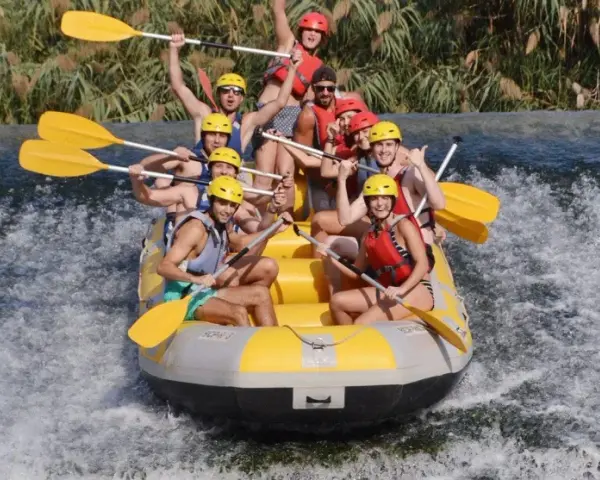 Un grupo de personas disfruta del rafting, remando con entusiasmo en una balsa amarilla sobre aguas turbulentas. ¡Una aventura emocionante!