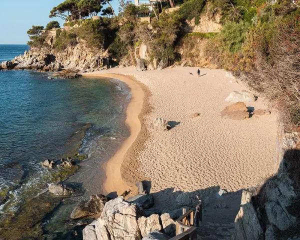 Una persona pasea por la cala belladona, con arena dorada y aguas cristalinas.