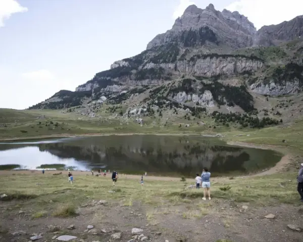 Gente paseando cerca de un lago en el valle de Tena, ideal para rutas de senderismo. Montañas escarpadas al fondo.