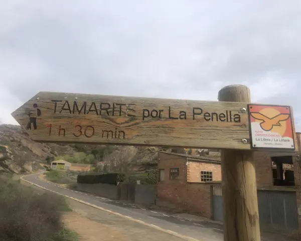 Señal de madera en albelda huesca: "Tamarite por La Penella, 1h 30 min". Al lado, señal de rutas ornitológicas.