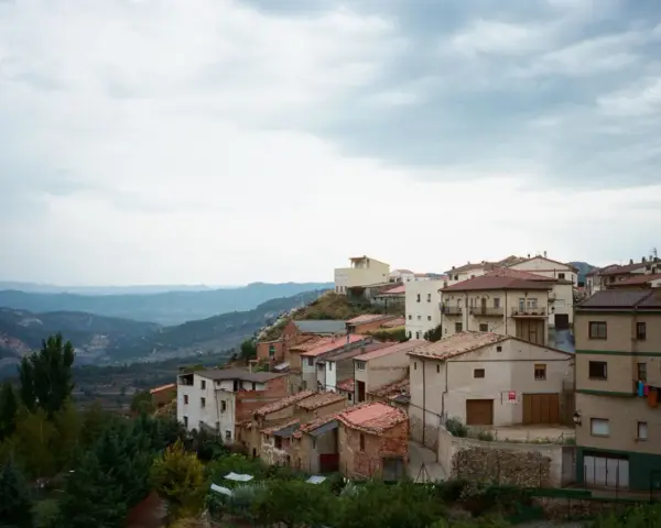 Pueblo español en ladera, con casas de tejados rojos y vistas a montañas. Se ven más de las matas verdes que rodean el asentamiento.