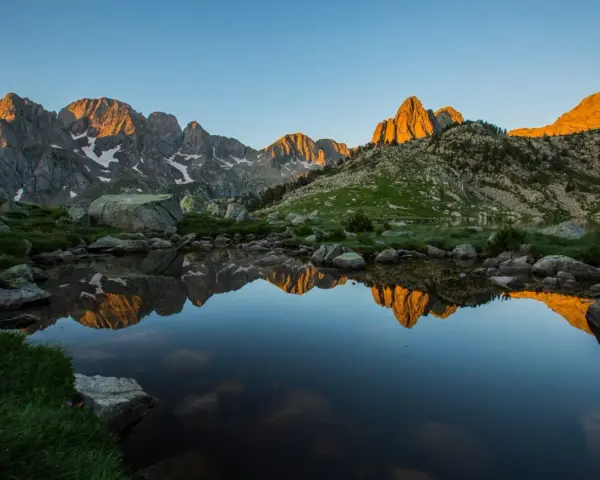 Reflejo dorado de montañas en un lago sereno del **parque natural Posets Maladeta** al amanecer.