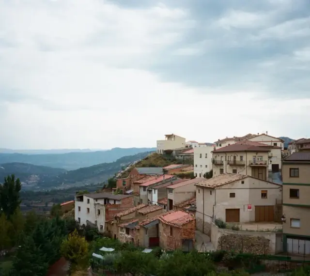Pueblo español en ladera, con casas de tejados rojos y vistas a montañas. Se ven más de las matas verdes que rodean el asentamiento.