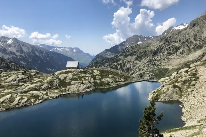 Un refugio solitario junto a los ibones de Bachimaña, rodeado de montañas rocosas y un lago azul intenso bajo un cielo despejado.