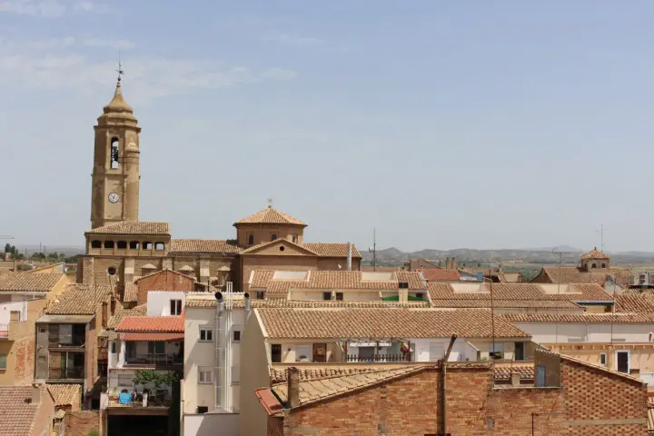 Vista aérea de un pueblo con tejados de teja, destacando una torre de iglesia con reloj. Hay mucho que ver en este pintoresco lugar.