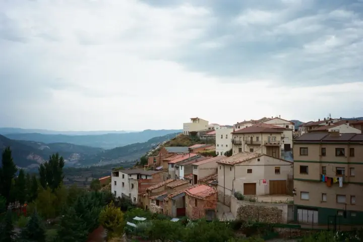 Pueblo español en ladera, con casas de tejados rojos y vistas a montañas. Se ven más de las matas verdes que rodean el asentamiento.