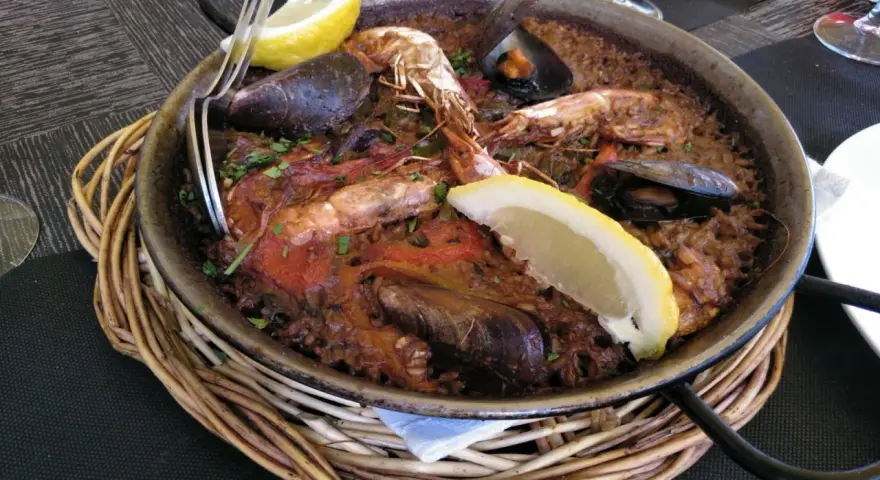 Paella marinera con gambas y mejillones, un plato típico de los restaurantes de Blanes, servida en una paellera sobre una cesta de mimbre.