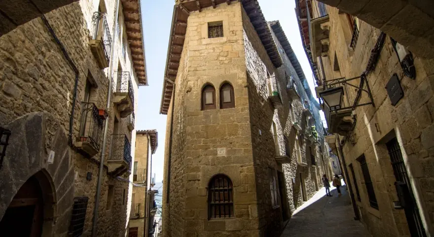 Calle empedrada con edificios de piedra, balcones de hierro y un arco. Un lugar que evoca la historia de los Reyes Católicos.