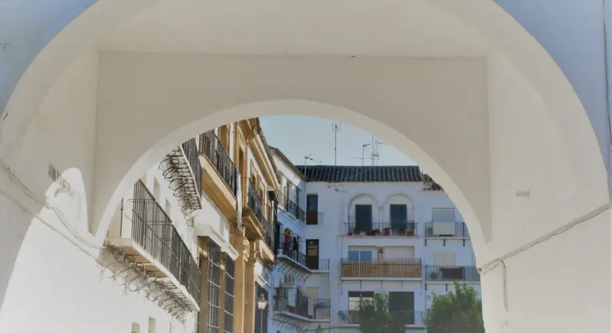 Un arco blanco enmarca edificios blancos y ocres con balcones de hierro forjado. Descubre qué ver en Marchena, un rincón andaluz lleno de encanto.