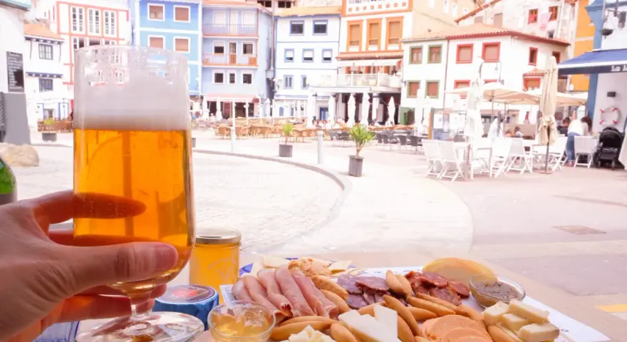 Disfrutando de una cerveza y una tabla de quesos y embutidos en Cudillero, con las coloridas casas de fondo.