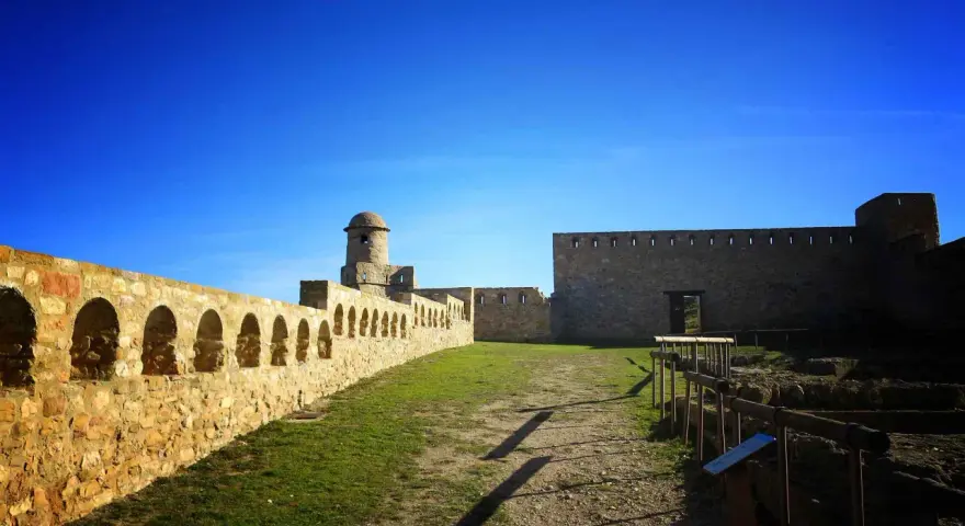 Impresionante castillo de piedra con murallas, arcos y torreón. Un lugar histórico que ver en Benabarre, bajo un cielo azul intenso.