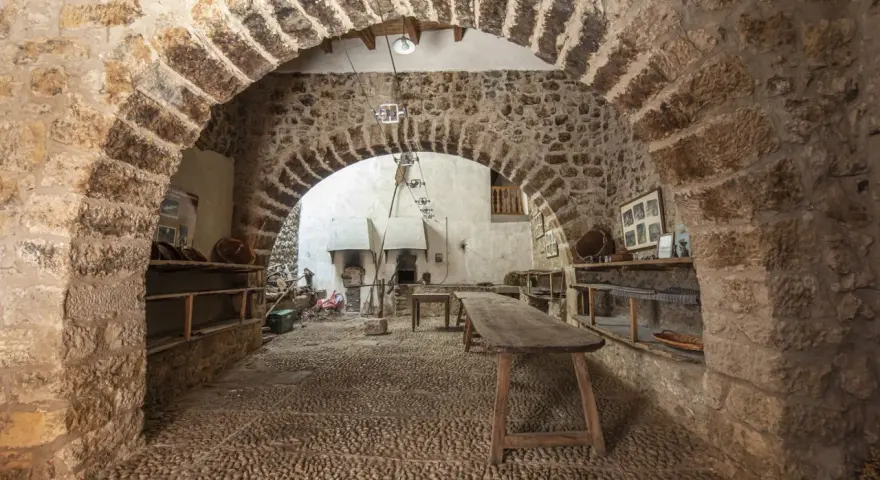 Interior de la torre de las arcas, con arcos de piedra, estanterías rústicas y un horno antiguo.