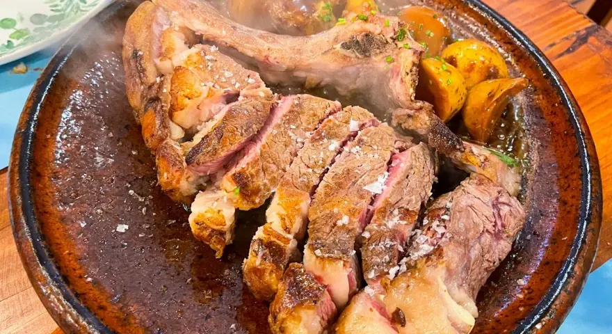 Un jugoso chuletón a la brasa, cortado y servido con patatas asadas, perfecto para comer en Tui.
