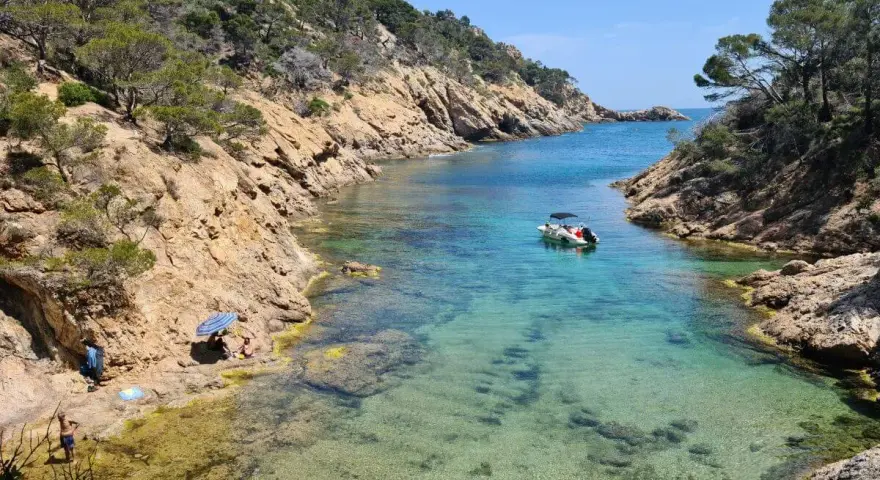 Una cala idílica en Tossa de Mar con aguas cristalinas, rocas escarpadas y un pequeño bote.