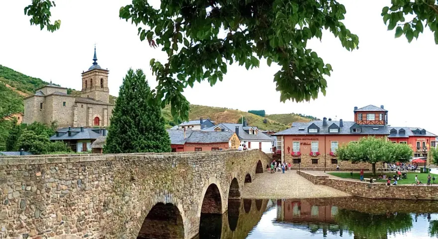 Puente romano y el pueblo de Molina Seca que ver. Iglesia antigua, casas y río con reflejos.