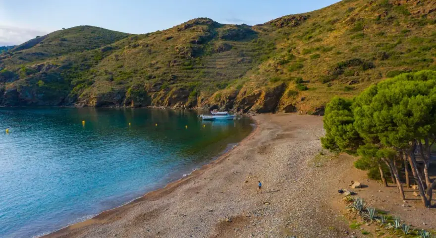 Tranquila cala Joncols plage con aguas turquesas, una persona paseando y barcas amarradas.