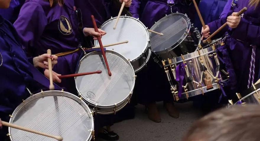 Tambores resonando, parte de las tradiciones de Aragón. Nazarenos con túnicas moradas golpean los parches en una procesión.