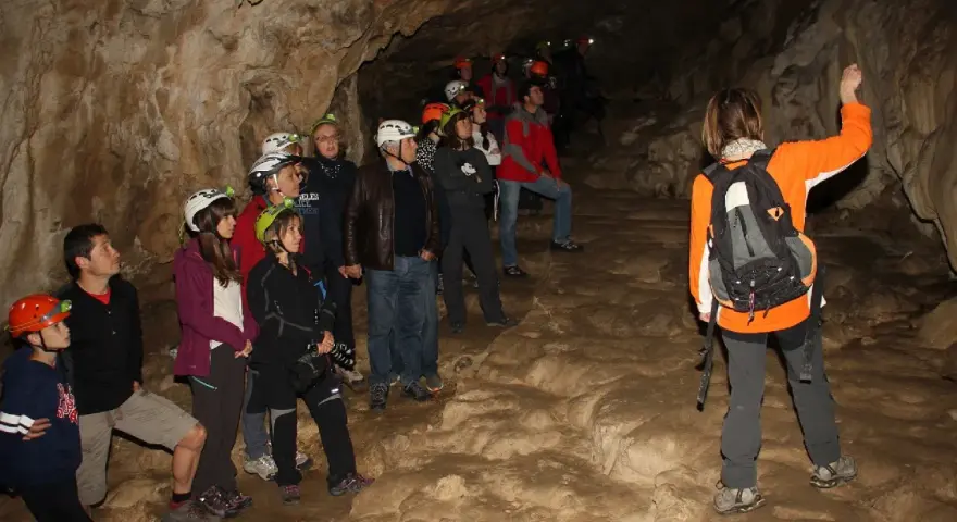 Grupo de exploradores con cascos y linternas en la cueva del oso, observando formaciones rocosas.