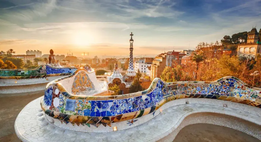 Bancos de mosaico coloridos en el Park Güell, un lugar imprescindible que ver en Barcelona, con la ciudad al amanecer.