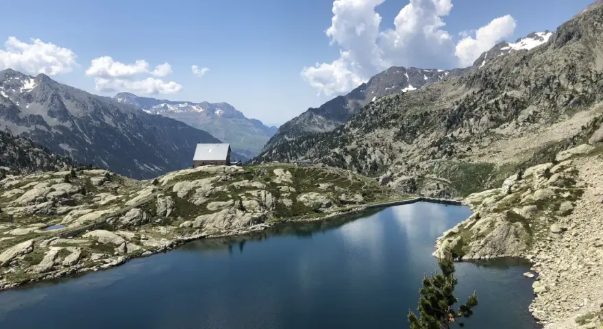 Un refugio solitario junto a los ibones de Bachimaña, rodeado de montañas rocosas y un lago azul intenso bajo un cielo despejado.