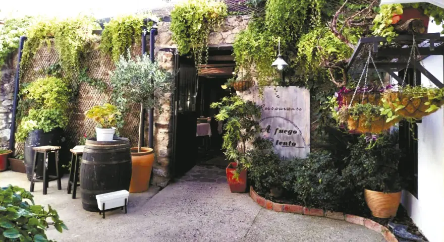 Entrada a un restaurante con vegetación exuberante. Un cartel dice "Restaurante A fuego lento". Ideal para saber donde comer en Hervás.