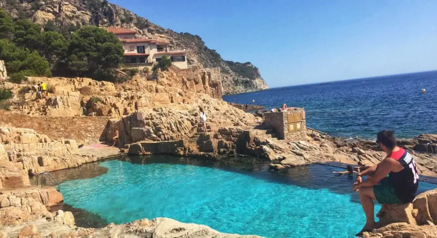 Piscinas naturales de Begur, con aguas cristalinas y rocas doradas. Un hombre contempla el mar azul.