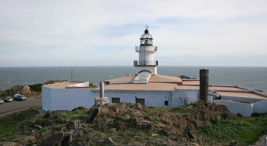 El faro de Cap de Creus se alza blanco y firme sobre rocas escarpadas, vigilando el mar azul.