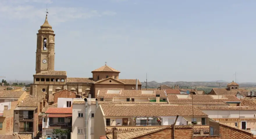Vista aérea de un pueblo con tejados de teja, destacando una torre de iglesia con reloj. Hay mucho que ver en este pintoresco lugar.