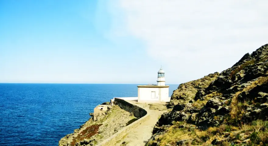 El faro de Cala Nans se alza sobre un acantilado rocoso, vigilando el azul intenso del mar Mediterráneo bajo un cielo despejado.