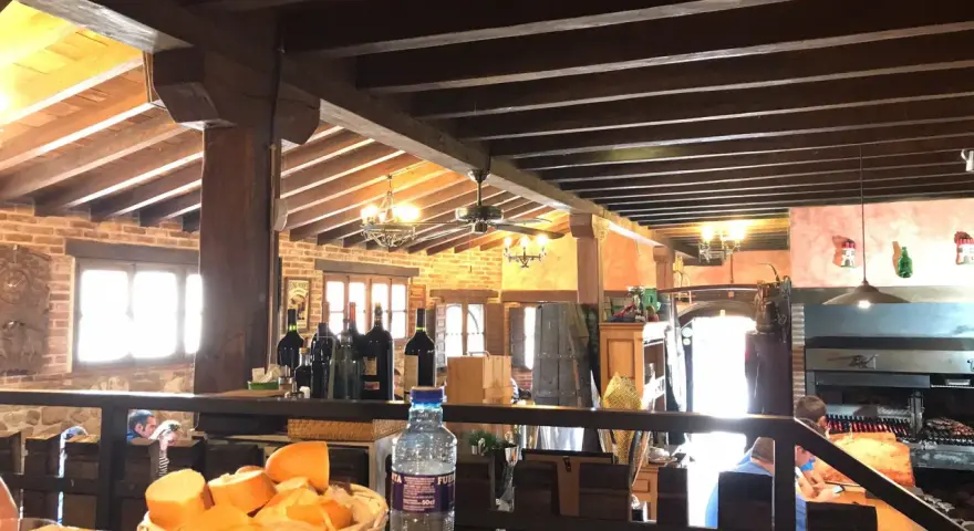 Interior rústico de restaurantes en Llanes, con vigas de madera, ladrillo y una parrilla a la vista. Cesta de pan y botella de agua en primer plano.